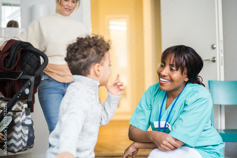 Boy talking to smiling female nurse while mother standing in background at medical clinic Boy talking to smiling female nurse while mother standing in background at medical clinic