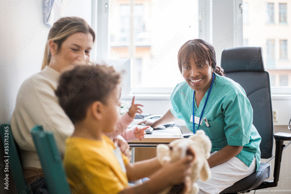 Smiling pediatrician talking to boy while mother sitting in clinic Smiling pediatrician talking to boy while mother sitting in clinic