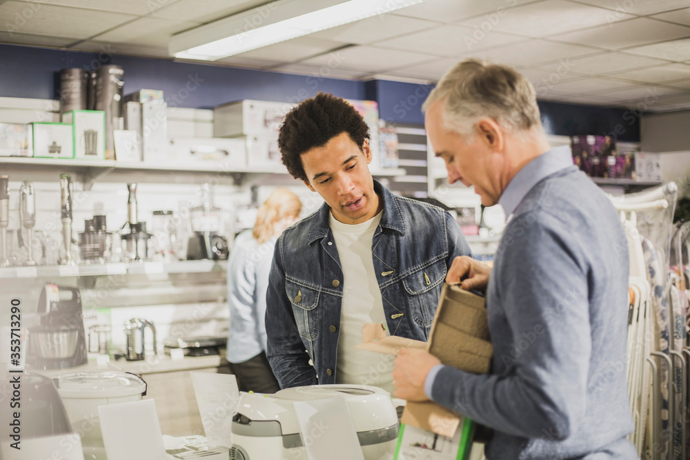 Mature salesman showing appliance to male customer in store Mature salesman showing appliance to male customer in store