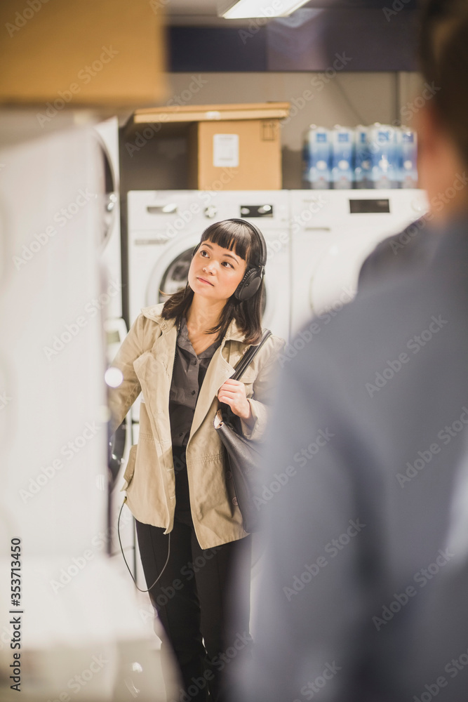 Young woman with headphones looking at appliances in electronics store Young woman with headphones looking at appliances in electronics store