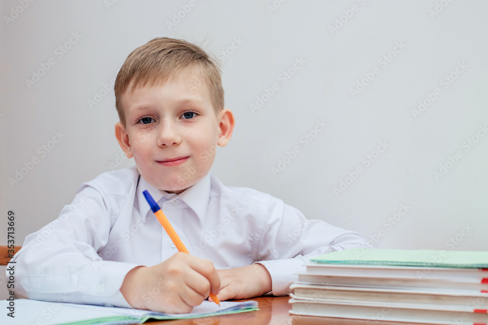 the boy is sitting at the table, holding a pen, next to notebooks and textbooks the boy is sitting at the table, holding a pen, next to notebooks and textbooks