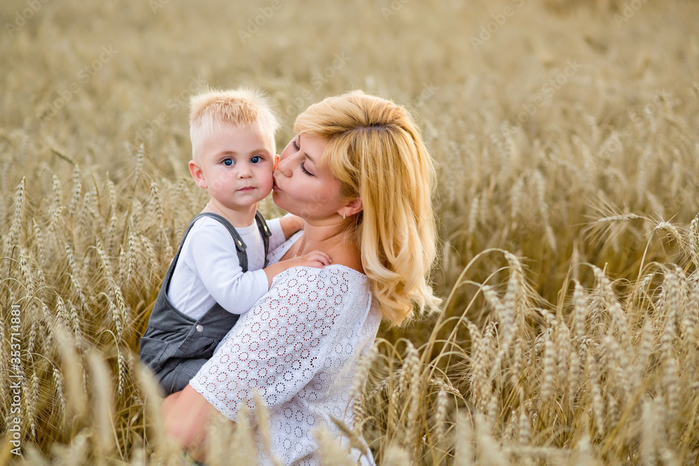 A beautiful blonde woman holds her blond son in her arms in a wheat field. She kisses him on the cheek. A beautiful blonde woman holds her blond son in her arms in a wheat field. She kisses him on the cheek.