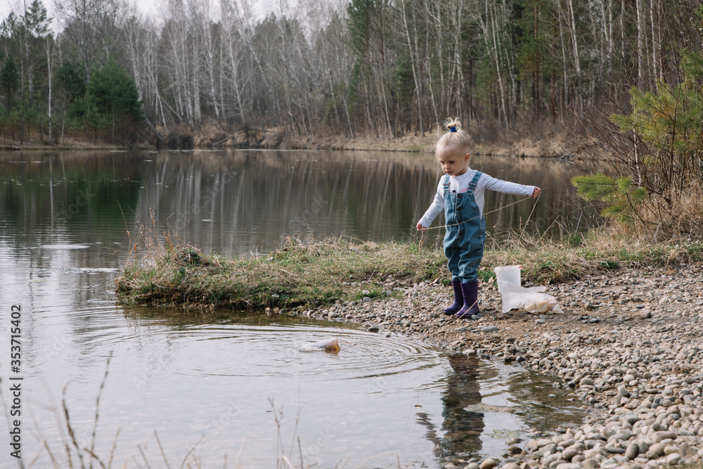 Little girl in rubber boots catches and feeds fish on the river in a jar