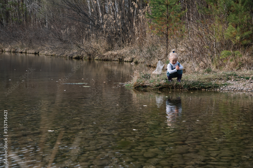 Little girl in rubber boots catches and feeds fish on the river in a jar Little girl in rubber boots catches and feeds fish on the river in a jar