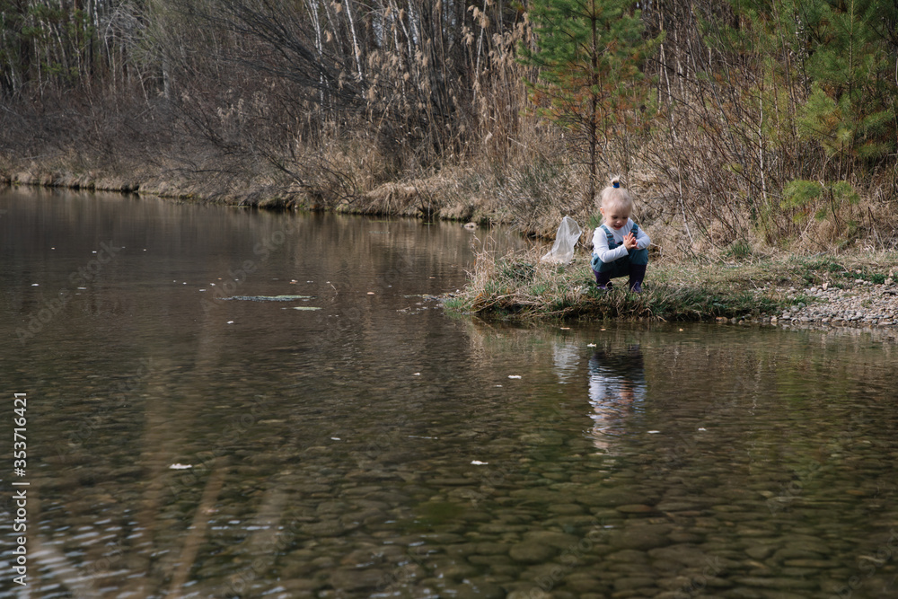 Little girl in rubber boots catches and feeds fish on the river in a jar