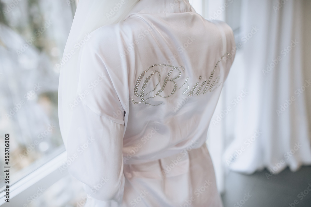 The bride in a white coat, lingerie stands with a beautiful inscription on her back. Photography, concept.