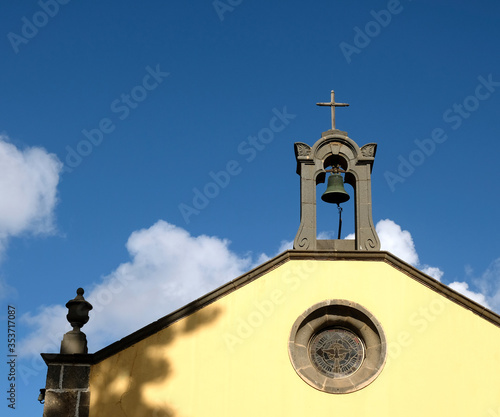 Church spire and bells atop of a church facade, with blue sky and a white cloud.
