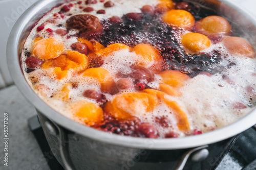 Fresh fruits are boiled in boiling water in a metal pan on a stove with bubbles and foam close-up. Cooking a delicious compote of apricot, apples, cherries, raspberries. Photography, concept.