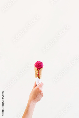 Raspberry ice cream cone on light brown background. Woman holding ice cream by hand. summer concept
