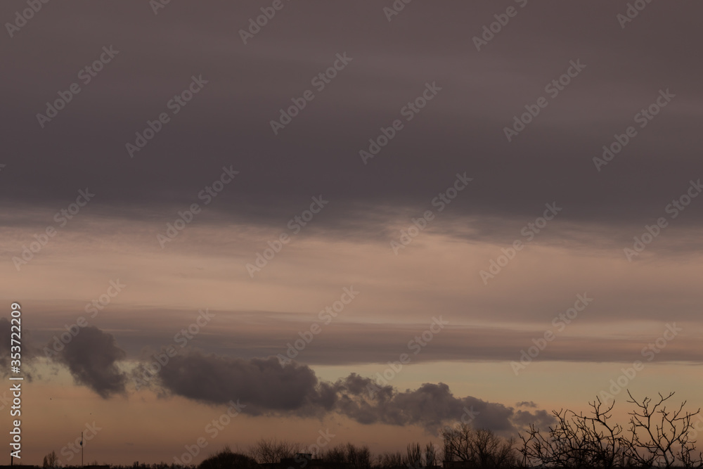Unusual rain clouds of different colors at sunset over the trees Unusual rain clouds of different colors at sunset over the trees