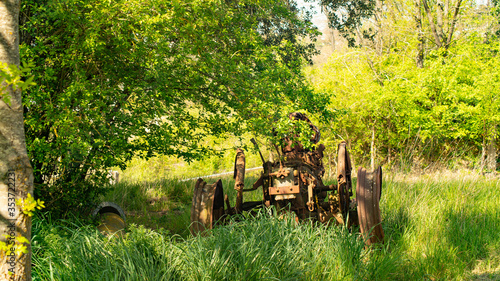  Agricultural machine at the foot of a large tree in a green field