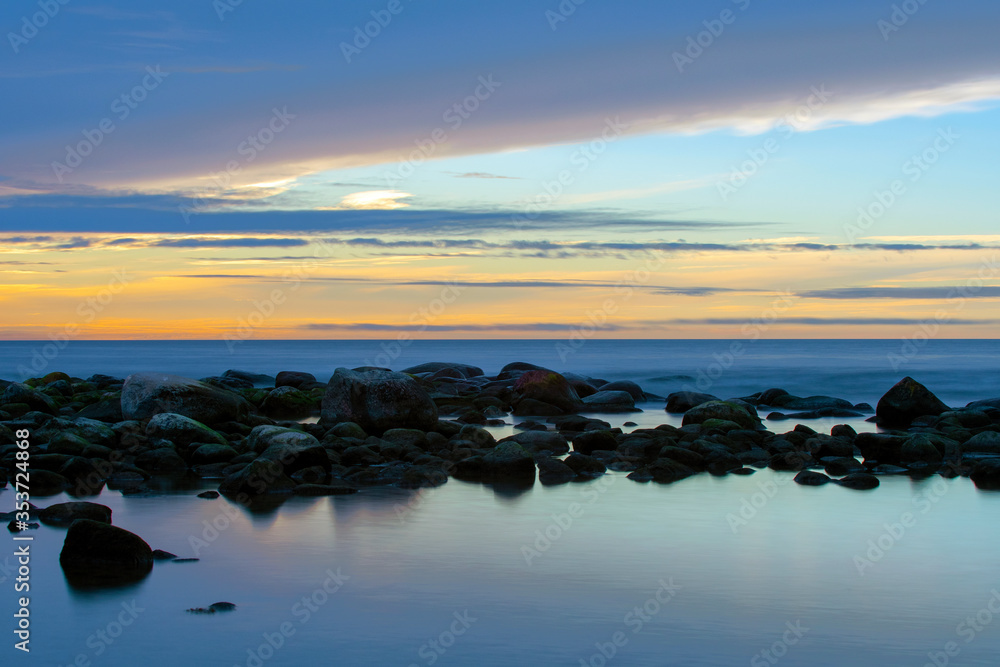 Naklejka premium Sunset Over Ocean With Stones In Foreground