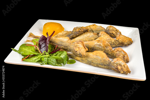 Gourmet Fried Trachurus with lemon and arugula on a plate, isolated on black background photo