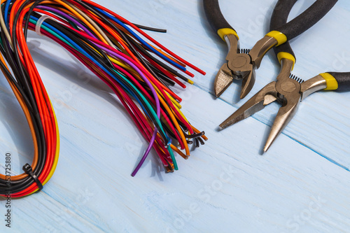 Pliers tools and multicolored wires for electrician closeup on blue boards