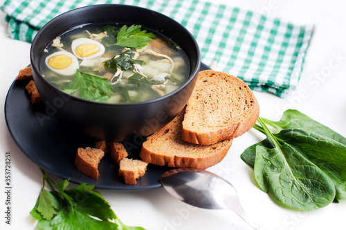 Green borsch with sorrel, parsley, egg and grens in black bowl with spoon on white background photo