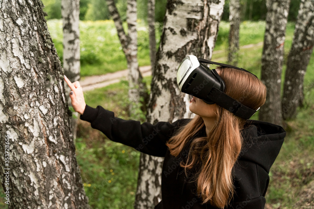 Fototapeta premium girl in virtual glasses touches a tree with a surprised face