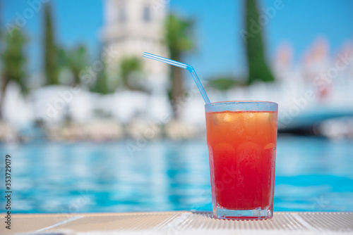 Fresh alcoholic red cocktail sex on beach with ice in glass on edge of pool in summer weather against background washed up pool and recreation area. Concept good holiday and travel  place for text.