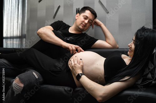 Romantic couple expecting baby, talking, enjoing and relaxing on sofa at home, free space. Pregnancy, maternity, preparation and expectation concept.