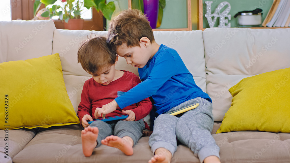 Two kids brothers smiling and happy playing together on the smartphone they are very pretty chatting each other in front of the camera Two kids brothers smiling and happy playing together on the smartphone they are very pretty chatting each other in front of the camera