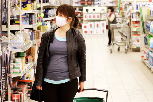Woman in medical mask in a mall on background of shelves with goods. Concept of shopping during quarantine at covid-19 pandemic