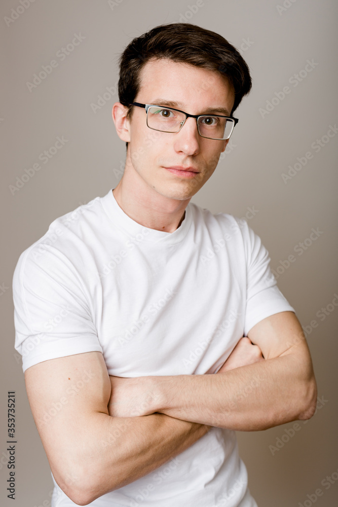 Young confident guy wearing glasses and a T-shirt sits on a gray background and looks at the camera calmly and thoughtfully. Young confident guy wearing glasses and a T-shirt sits on a gray background and looks at the camera calmly and thoughtfully.