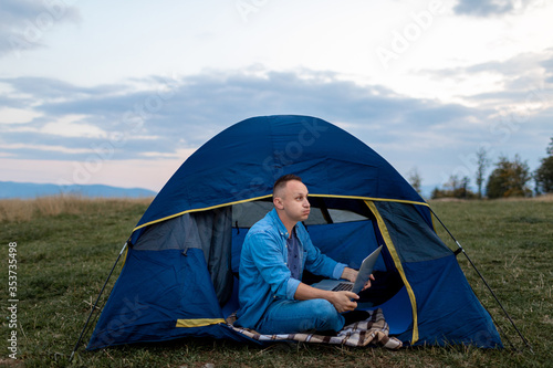 male freelancer is working on a laptop outdoors in mountains. Freelance concept.