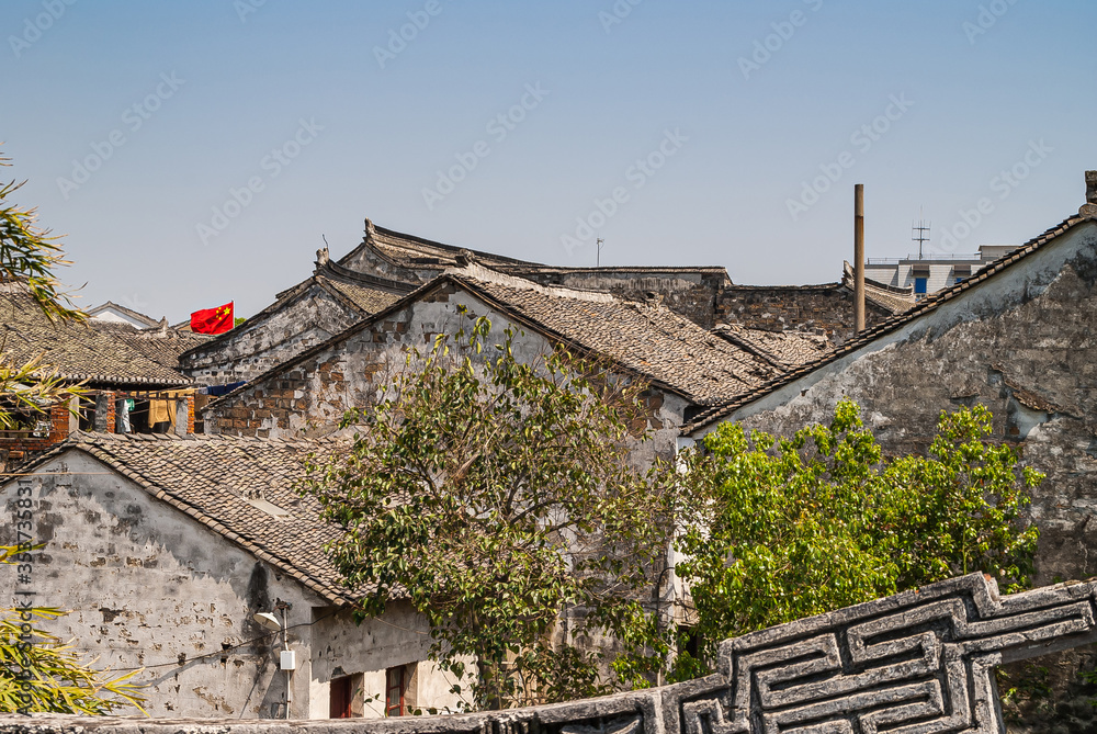 Tongli, JIangsu, China - May 3, 2010: Red Chinese flag waves above Chinese architecture gray roof under light blue sky.