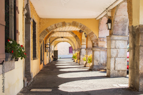 Medieval arches with flowers and lantern. Empty archway in France. Yellow arcade on sunny day. Ancient european architecture. Corridor with arches in old village building horizontal. Travel concept.  © Nataliia