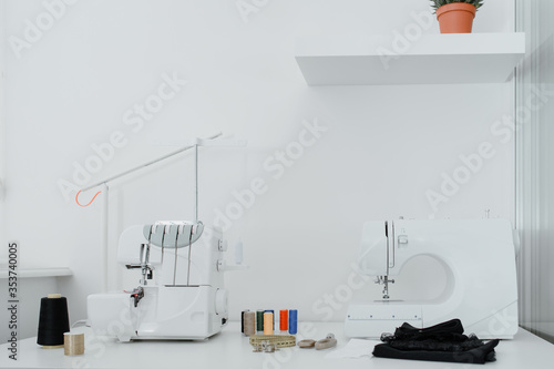 Close up sewing and overlock machines, spool of thread, scissors, centimeter ribbon and pieces of black material on the table photo