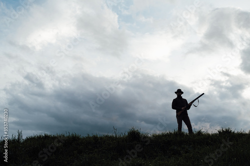 Vintage hunter walks. Rifle Hunter Silhouetted in Beautiful Sunset or Sunrise. Hunter aiming rifle in swamp and field