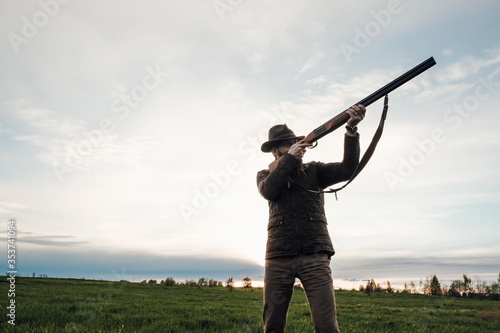 Vintage hunter walks. Rifle Hunter Silhouetted in Beautiful Sunset or Sunrise. Hunter aiming rifle in swamp and field