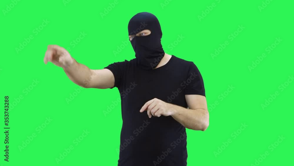 A masked man manages the situation, showing with his hands what to do.Balaclava.Green screen background. A masked man manages the situation, showing with his hands what to do.Balaclava.Green screen background.