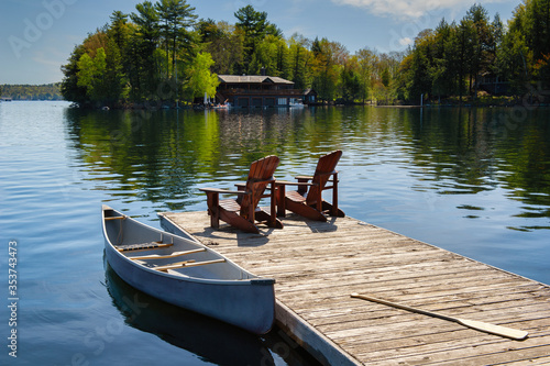 Two Muskoka chairs sitting on a wood dock facing a lake Fototapet