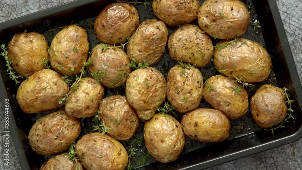 Oven baked whole potatoes with seasoning and herbs in metalic tray. Roasted potatoes in jackets. Oven baked whole potatoes with seasoning and herbs in metalic tray. Roasted potatoes in jackets.