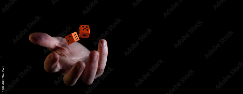 Two orange dice cubes thrown in the air above caucasian male hand against black background - narrow banner with copy space Two orange dice cubes thrown in the air above caucasian male hand against black background - narrow banner with copy space