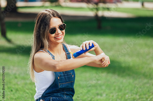 Young woman applying sunscreen or insect repellent outdoors in public park.