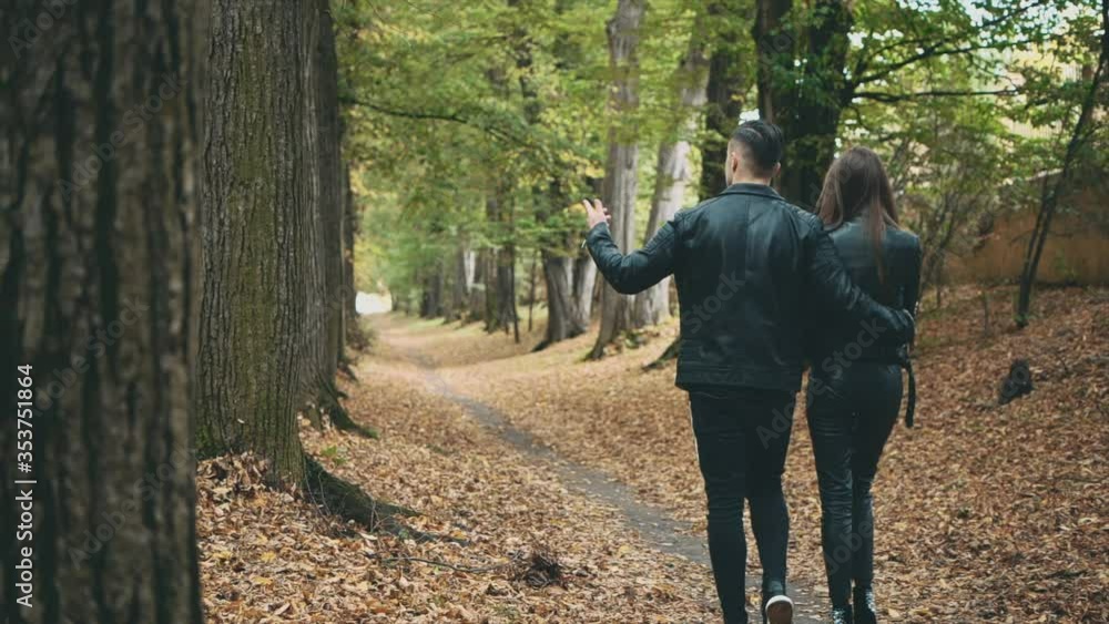 A loving couple walks in autumn park. Back view. Strong guy is hugging is girlfriend. Slow motion. Copy space. 4K.
