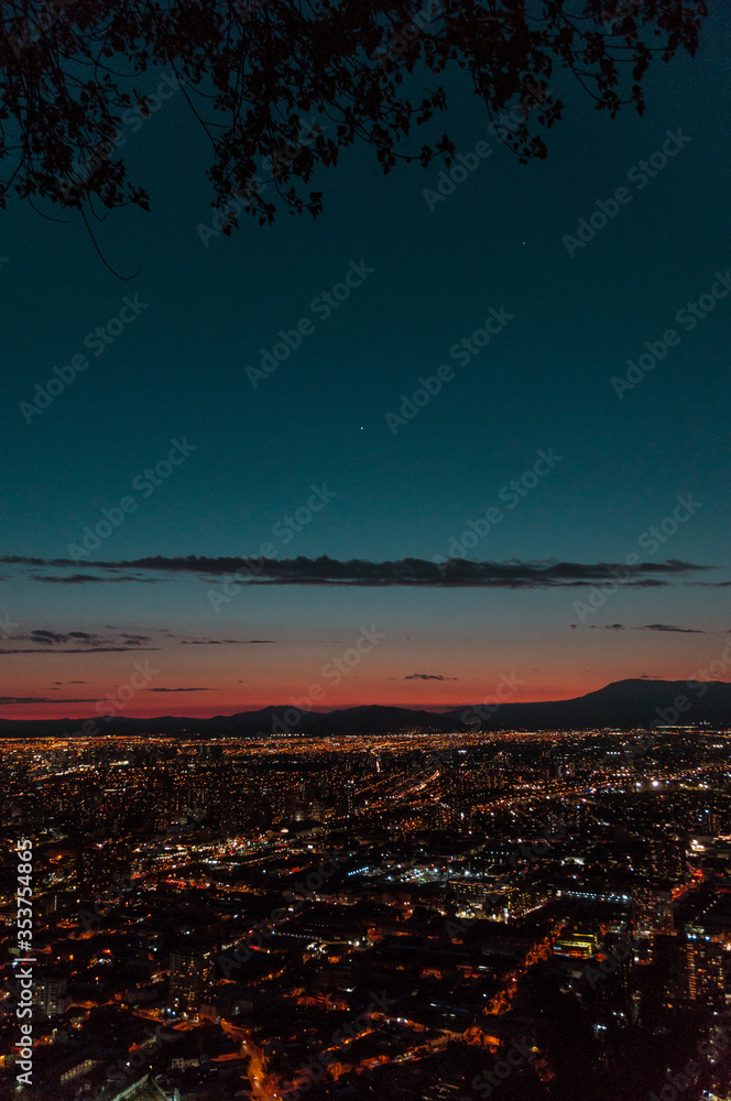 Ciudad de noche con luces encendidas entre montañas en el horizonte, foto vertical
