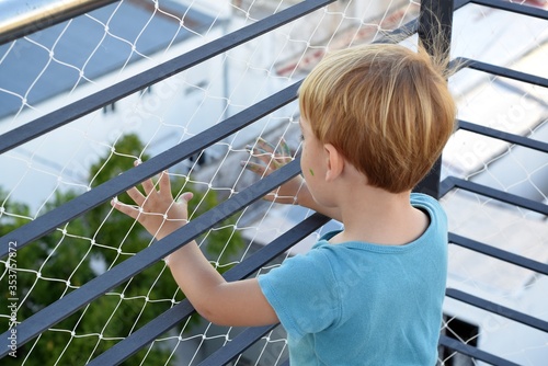 Two years old blond boy playing at the terrace during quarantine for coronavirus. There is a security net on the balcony. 21st March, 2020, Buenos Aires, Argentina.