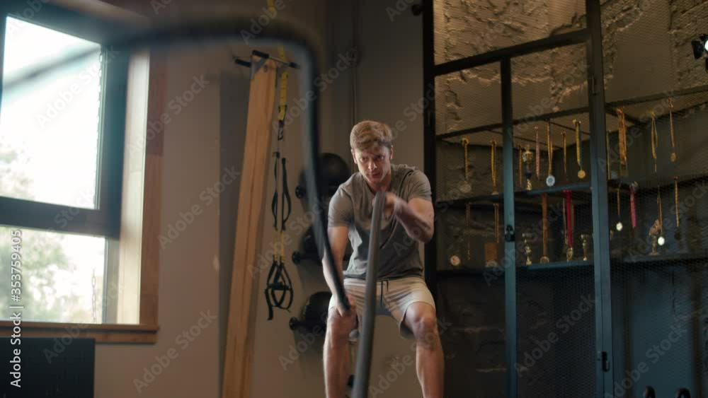 Strong sportsman using battle ropes in fitness center. Man training at gym Strong sportsman using battle ropes in fitness center. Man training at gym