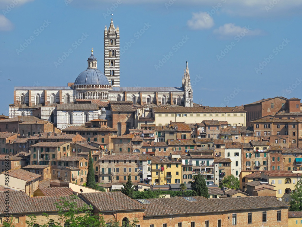 The cityscape of Siena, Italy, with the Siena Cathedral in the background, is shown during the day.