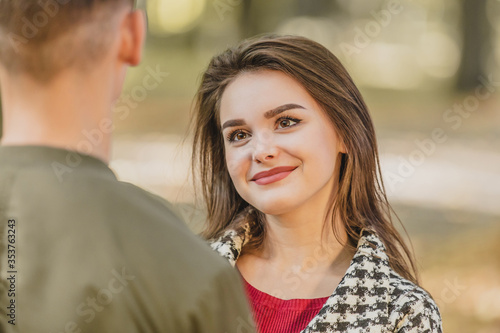 Adorable young woman is looking at her boyfriend, standing back to the camera, with big admiration and appreciation.