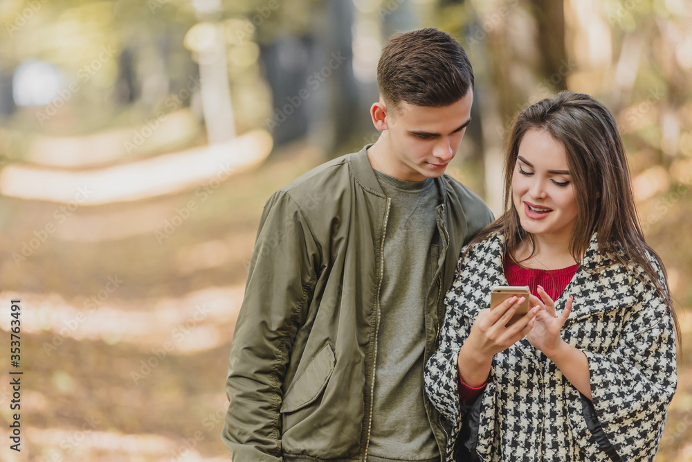 Fototapeta premium Copyspace photo of cheerful girl, showing photos to her boyfriend, while they are spending free time in autumn park.