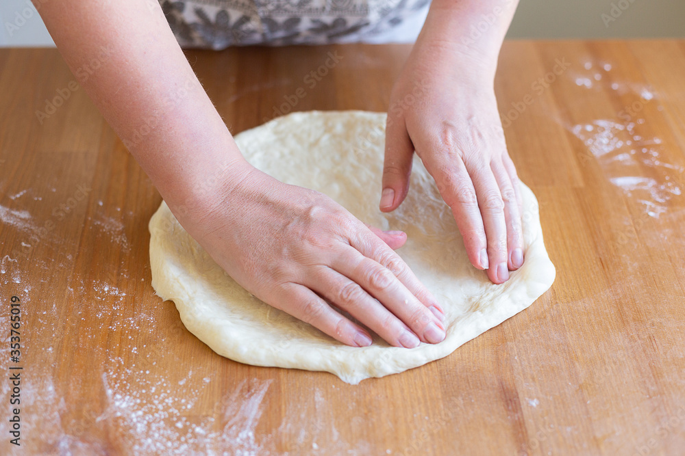 Wooman is making homemade pizza for the family. Hands of a woman roll out the dough in the home kitchen, daylight. The process of making fresh homemade elastic dough for baking pizza or pie. Easy cook