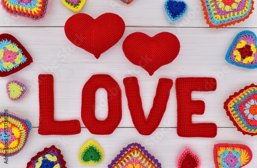 Knitted hearts and the word love are placed on white wooden boards.