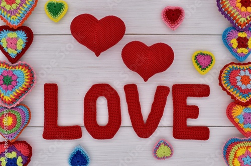 Knitted hearts and the word love are placed on white wooden boards.