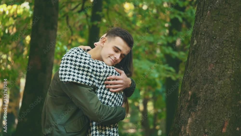 Young, adorable girl is waiting for her boyfriend near a tree, being on blurred autumn background. Guy is hugging her firmly. Close up. 4K. Young, adorable girl is waiting for her boyfriend near a tree, being on blurred autumn background. Guy is hugging her firmly. Close up. 4K.