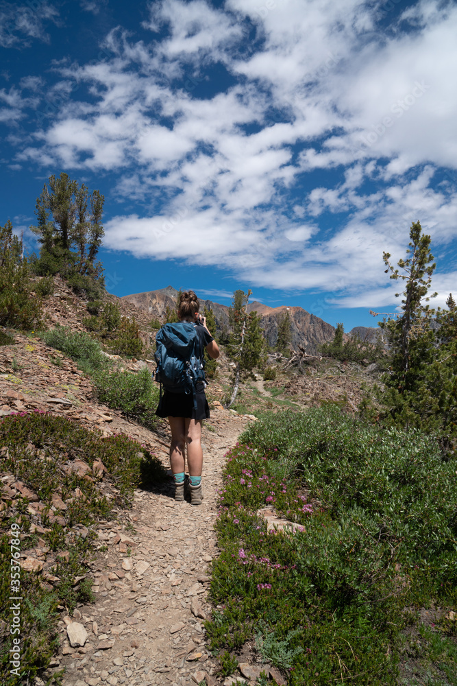 Beautiful female backpacker hiker takes photos along the trail in California's eastern sierra nevada along 20 Lakes Basin Hike on a sunny summer day