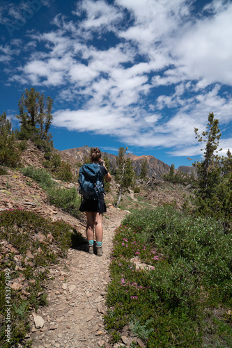 Beautiful female backpacker hiker takes photos along the trail in California's eastern sierra nevada along 20 Lakes Basin Hike on a sunny summer day