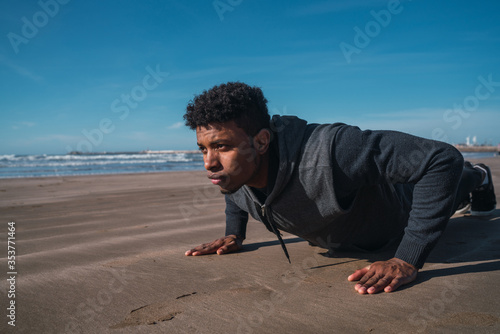 Athletic man doing push-ups at the beach. © Mego-studio
